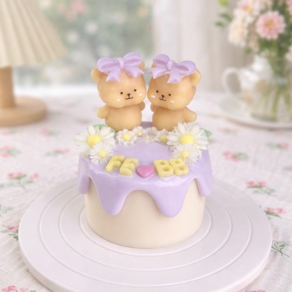 A lilac cake candle decorated with flowers and two little bears